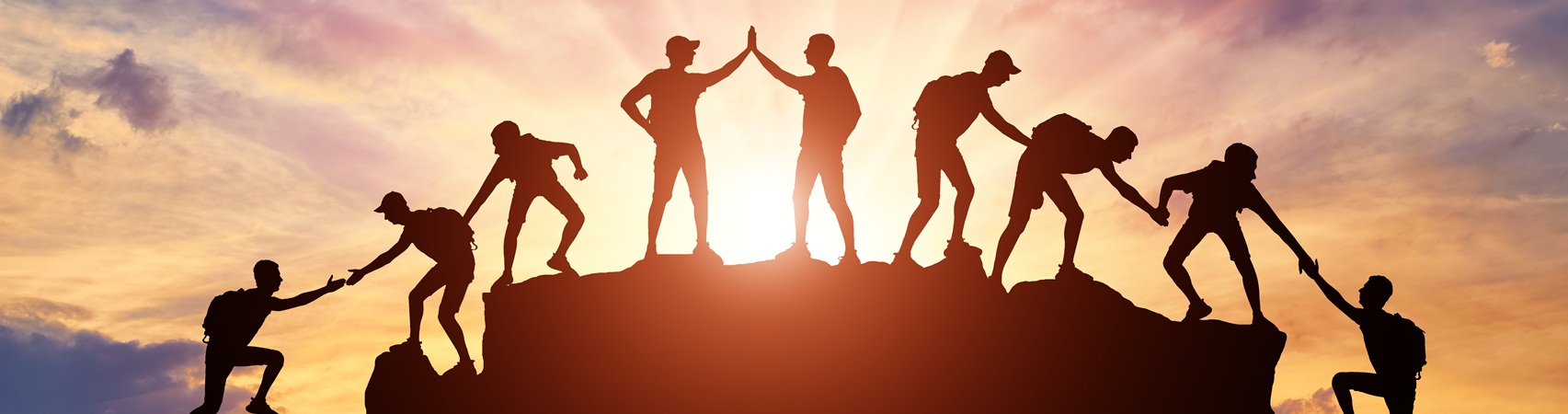 Silhouette of climbers who climbed to the top of the mountain thanks to mutual assistance and teamwork